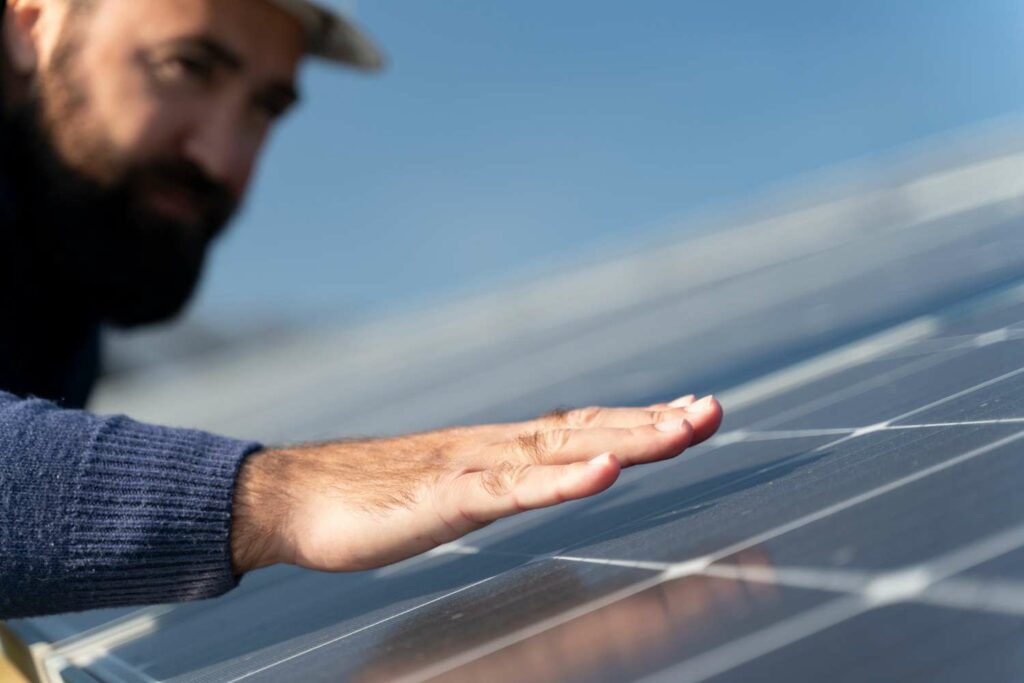 homme place sa main au dessus d'un panneau solaire